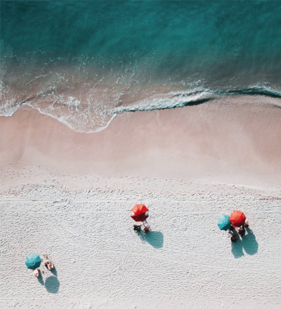 Ein Strand aus der Vogelperspektive mit Meeresbrandung und vier Sonnenschirmen.
