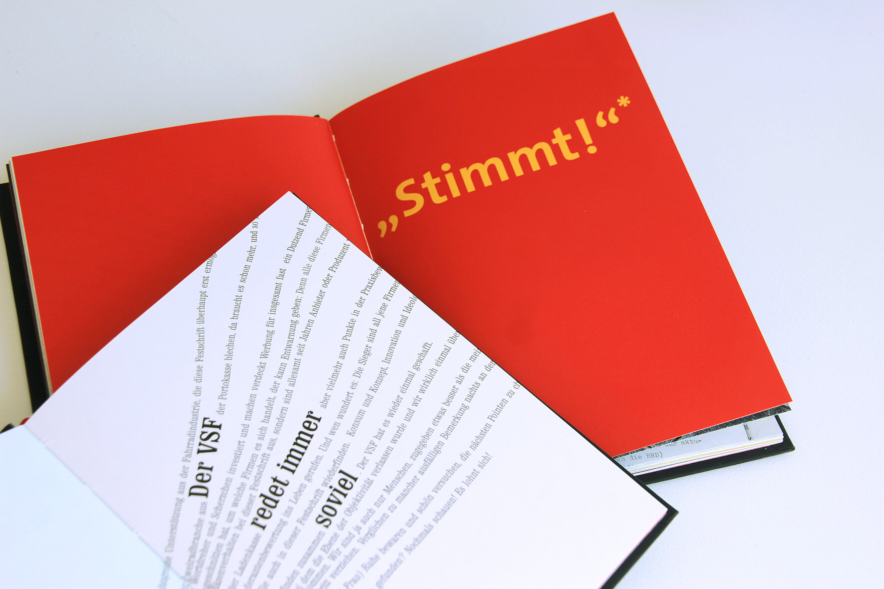 Zwei übereinanderliegende, aufgeschlagene Bücher. Eine Doppelseite ist rot mit gelbem Schriftzug, die andere ist mit frei gesetzter Typografie gestaltet.  