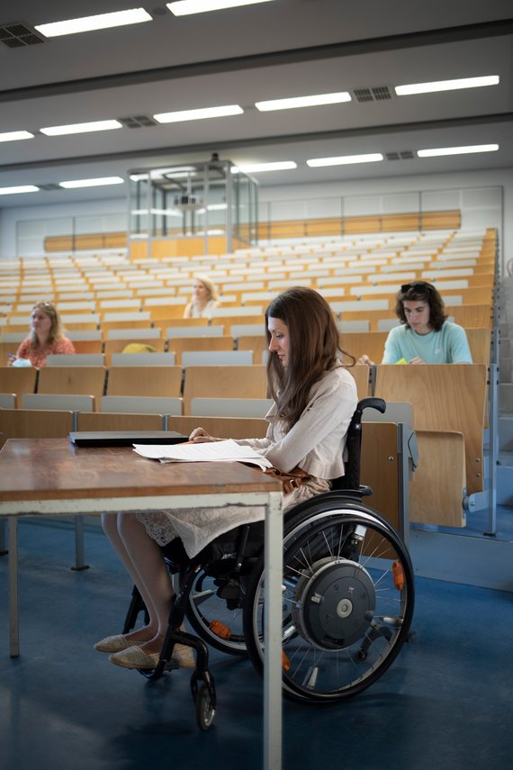 Eine Frau im Rollstuhl nimmt an einer Vorlesung in der Universität Heidelberg teil.