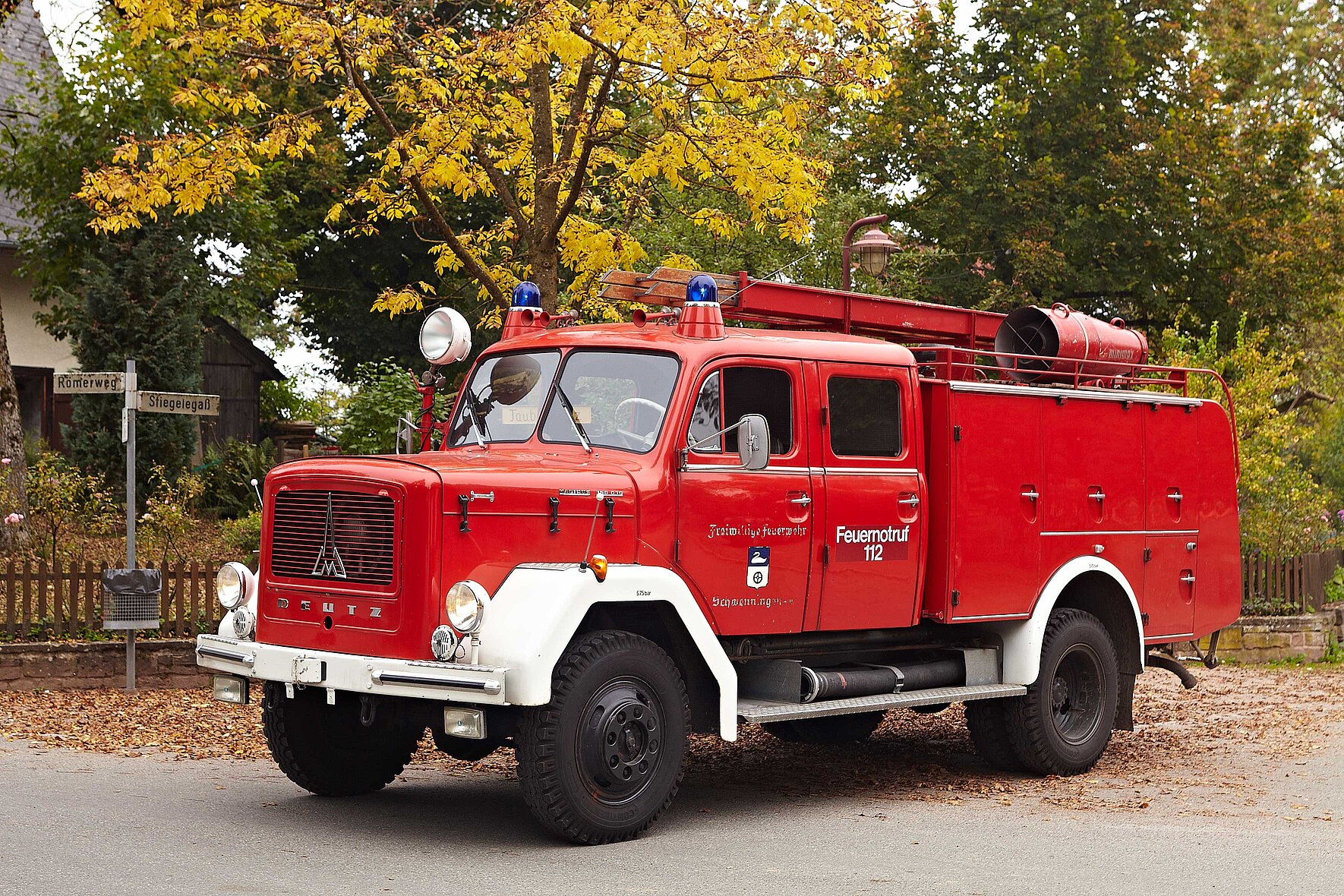 Ein altes Feuerwehrauto der freiwilligen Feuerwehr Peterzell vor einem Haus mit Garten.